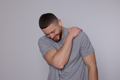 Man suffering from pain in his shoulder on light grey background. Arthritis symptom