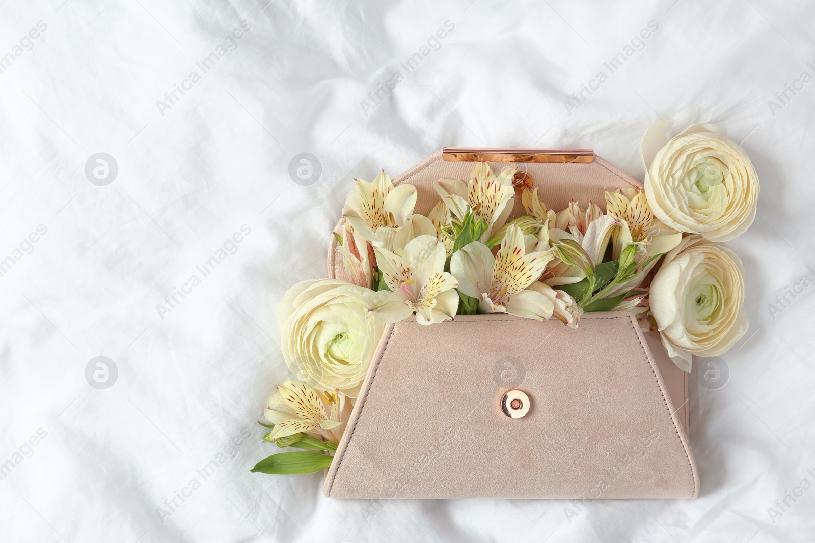 Photo of Stylish clutch with spring flowers on crumpled sheet, top view. Space for text