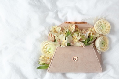 Photo of Stylish clutch with spring flowers on crumpled sheet, top view. Space for text