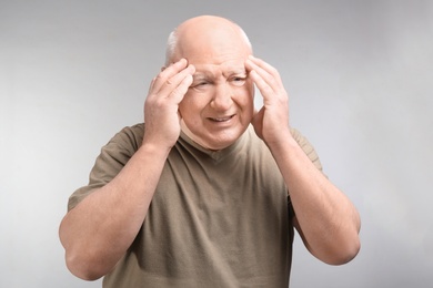 Photo of Senior man suffering from headache on light background. Enduring pain