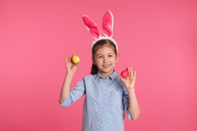 Photo of Little girl in bunny ears headband holding Easter eggs on color background