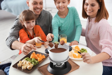 Photo of Happy family enjoying fondue dinner at home, selective focus