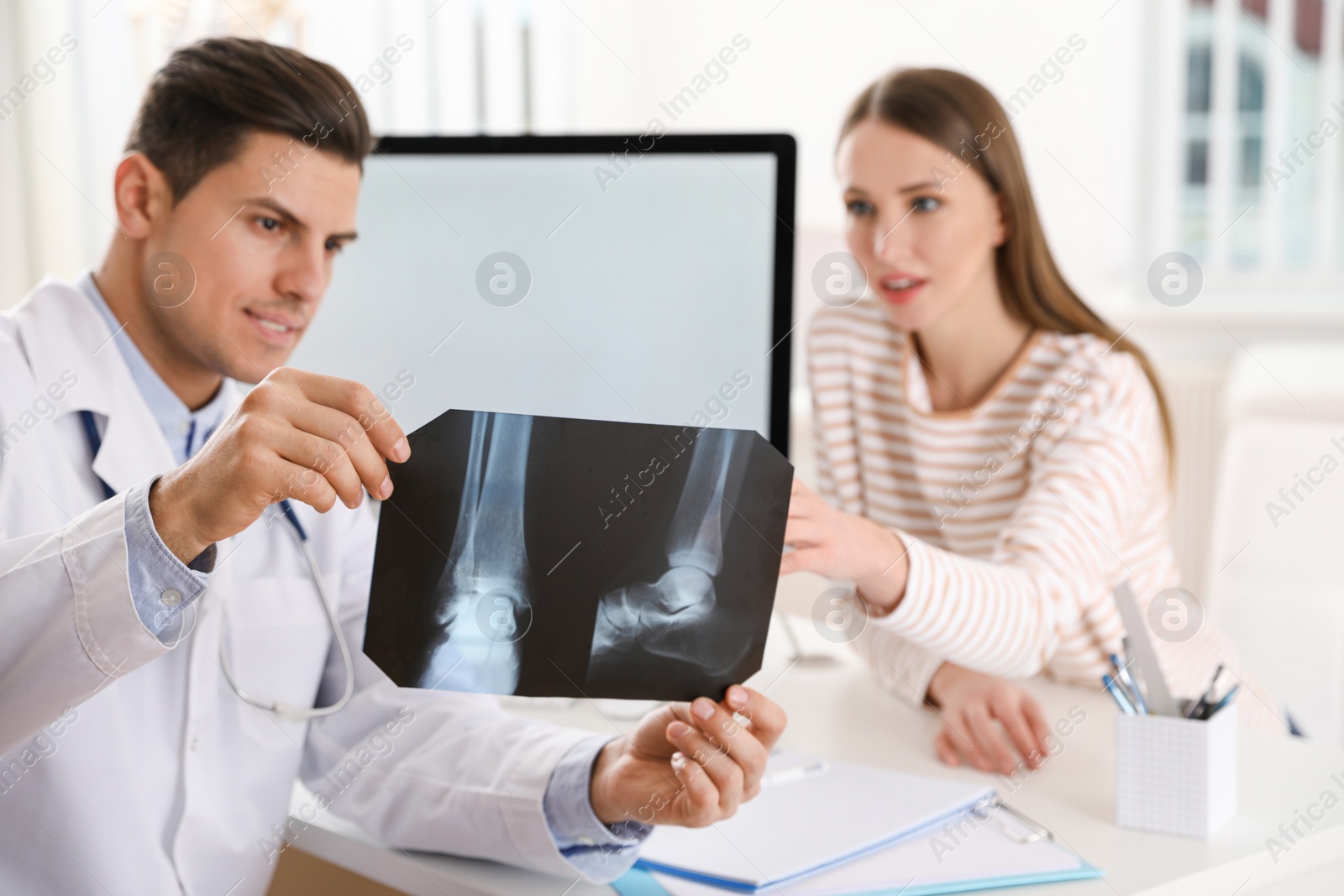 Photo of Orthopedist showing X-ray picture to patient at table in clinic