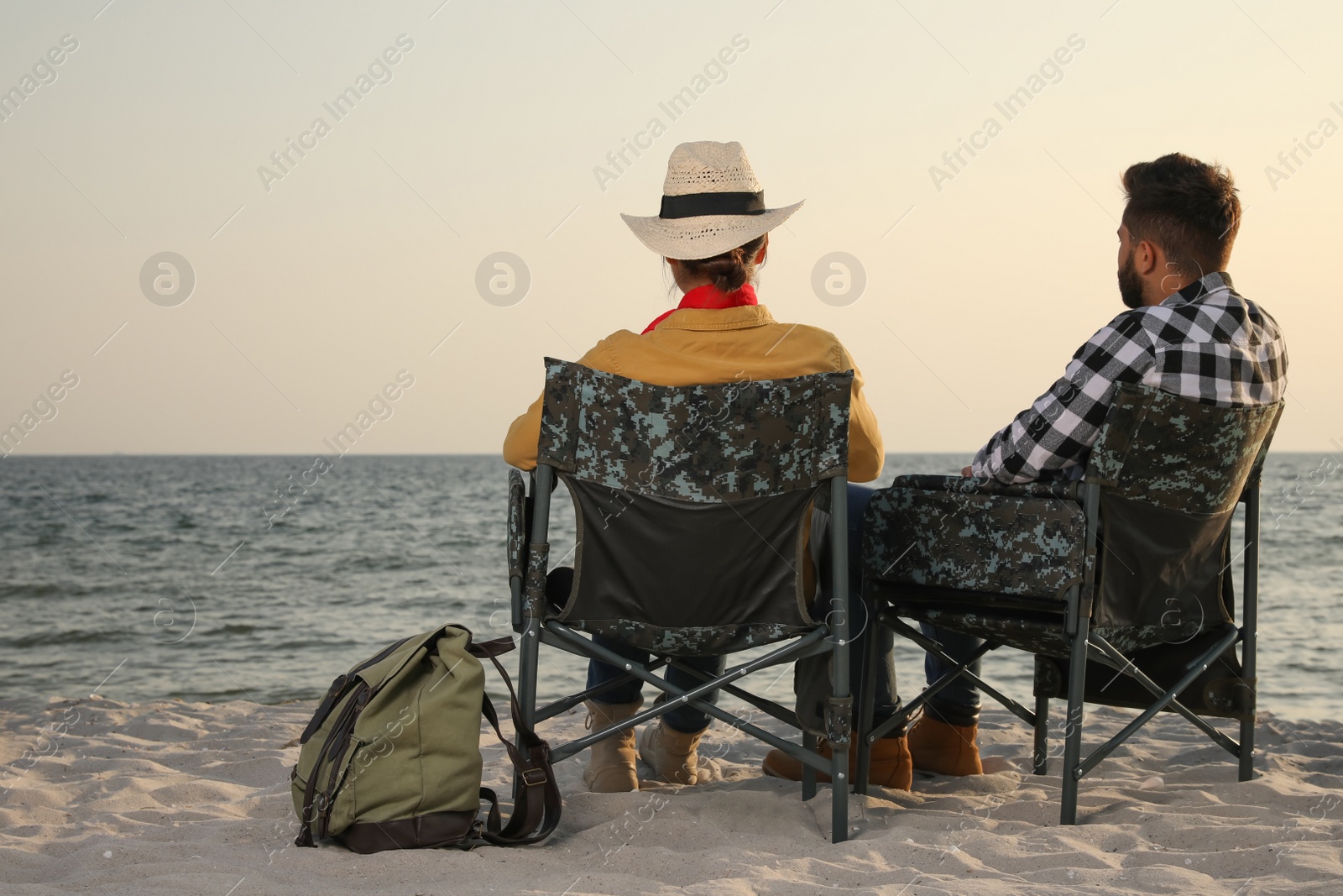 Photo of Couple sitting in camping chairs and enjoying seascape on beach, back view