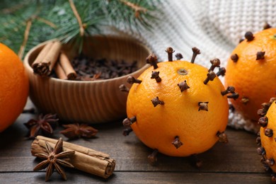 Pomander balls made of tangerines with cloves and fir branches on wooden table, closeup