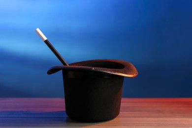 Photo of Magician's hat and wand on wooden table against blue background