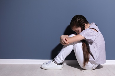Photo of Depressed little girl sitting on floor indoors. Time to visit child psychologist