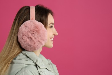 Happy woman wearing warm earmuffs on pink background, space for text