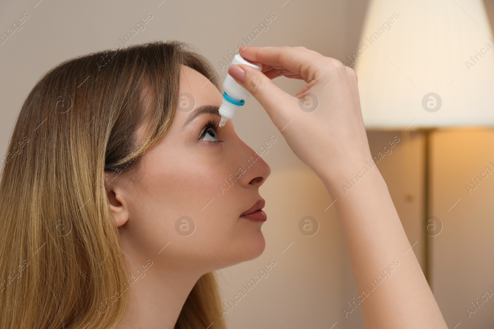 Photo of Young woman using eye drops at home