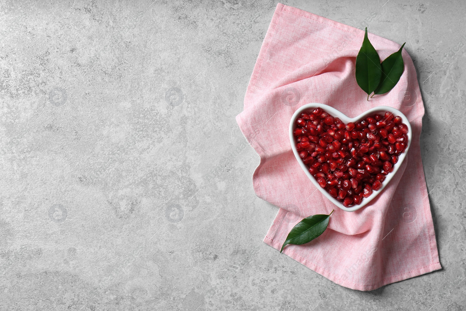 Photo of Heart shaped bowl of pomegranate seeds on grey background, top view with space for text