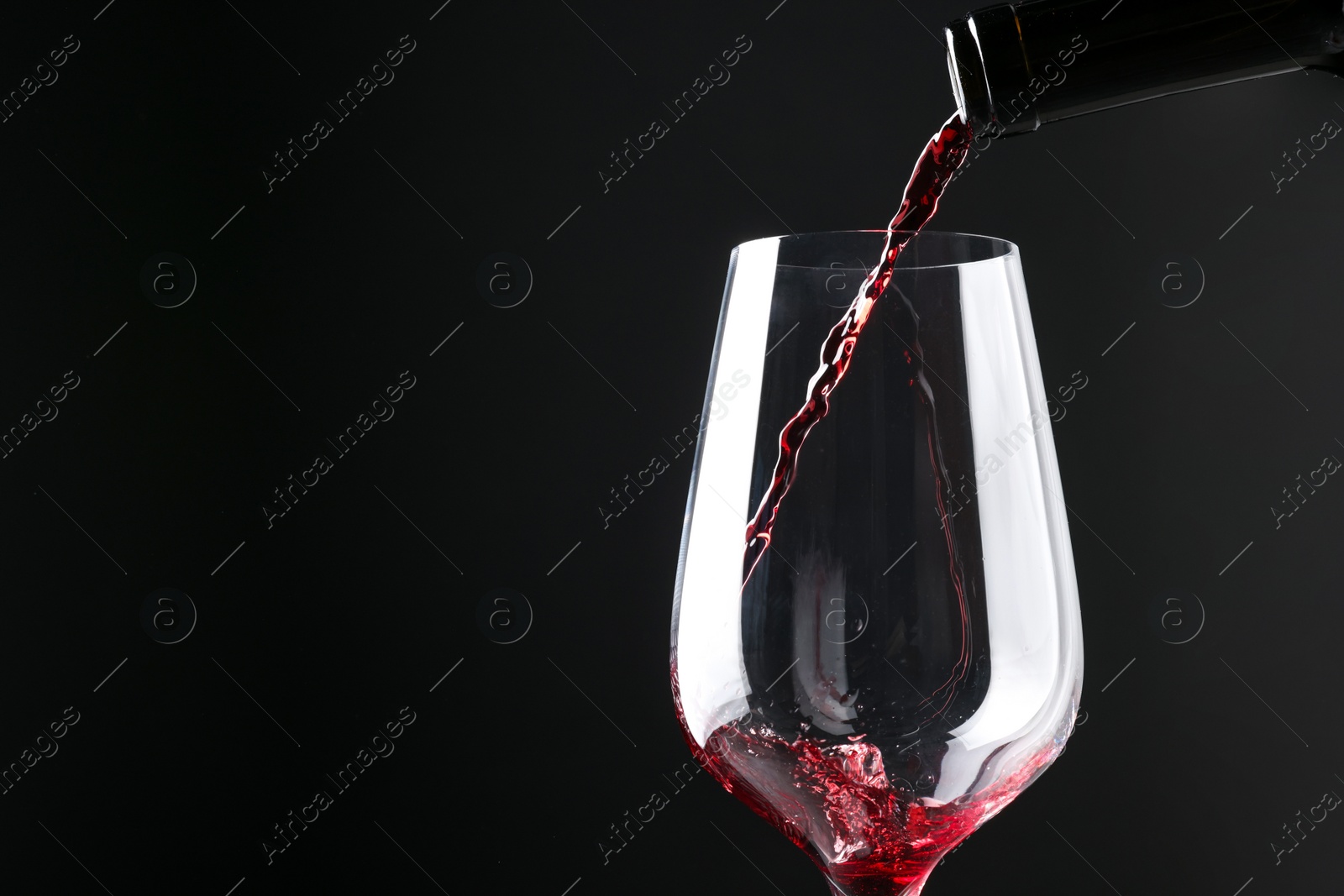 Photo of Pouring red wine into glass against black background, closeup. Space for text