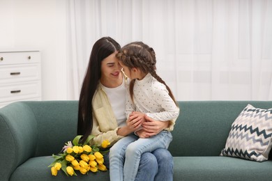 Photo of Happy woman and her cute daughter with bouquet of yellow tulips on sofa at home. Mother's day celebration