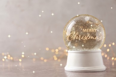 Image of Beautiful snow globe with phrase Merry Christmas on marble table against festive lights, space for text