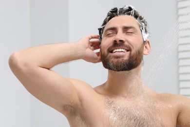 Photo of Happy man washing his hair with shampoo in shower