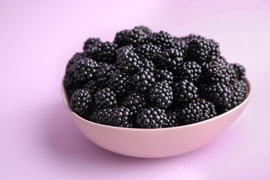 Photo of Fresh ripe blackberries in bowl on light violet background