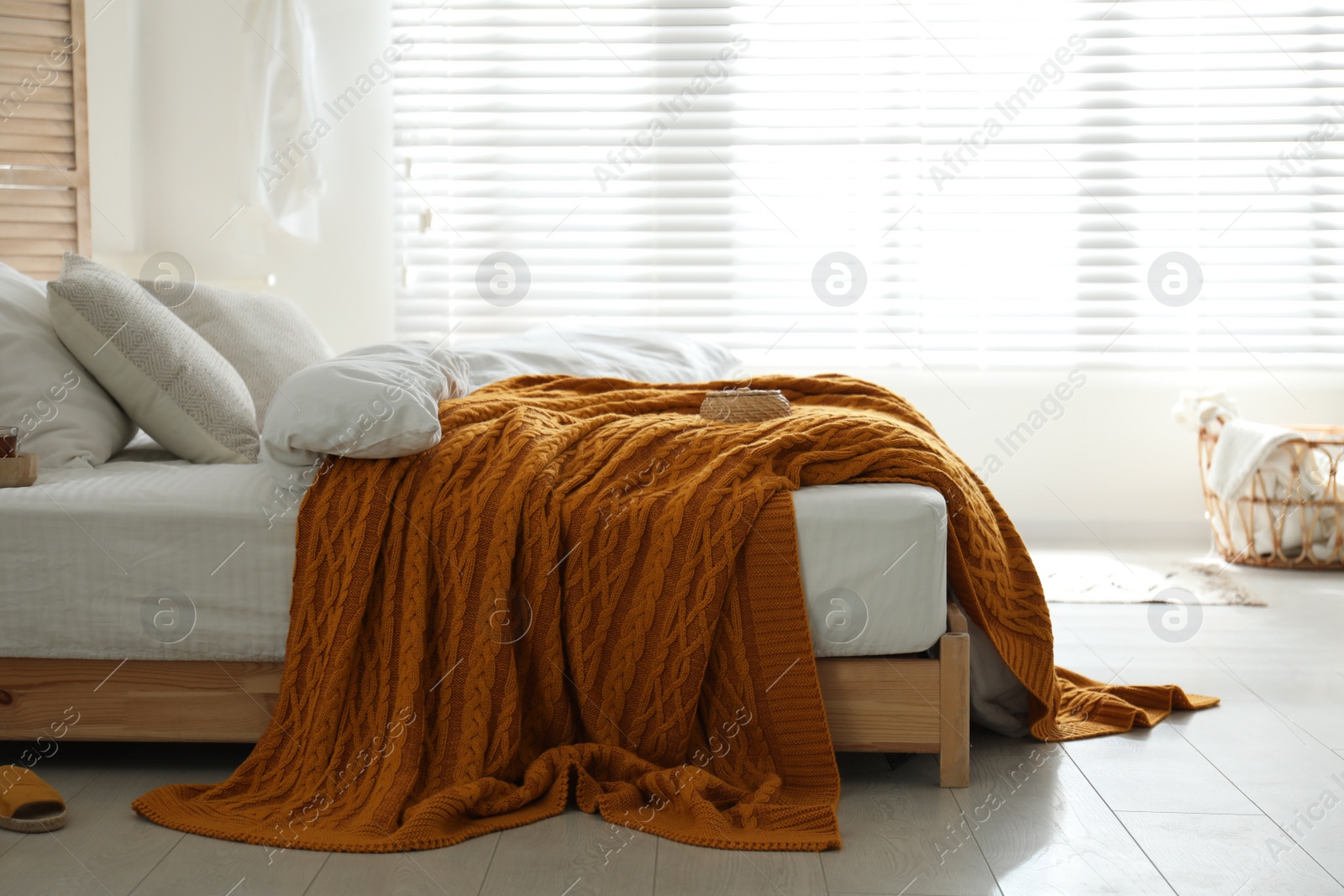 Photo of Comfortable bed with warm knitted plaid in stylish room interior