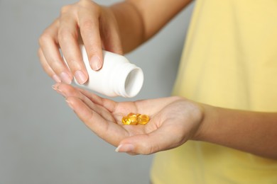 African-American woman with bottle of vitamin capsules on light grey background, closeup