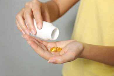 Photo of African-American woman with bottle of vitamin capsules on light grey background, closeup