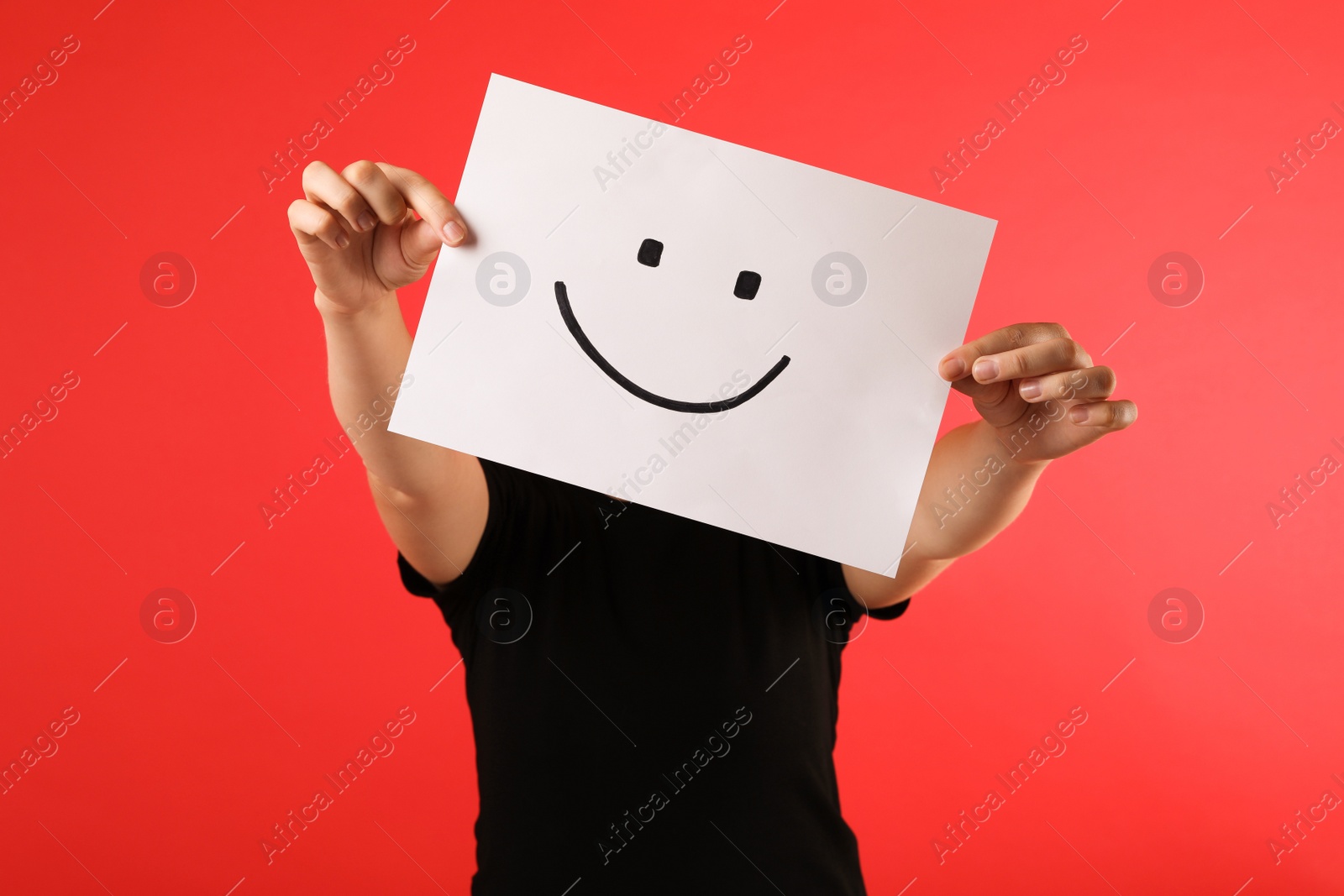 Photo of Woman hiding behind sheet of paper with happy face on red background