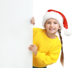 Photo of Happy child in Santa hat peeping out of blank banner on white background. Christmas celebration