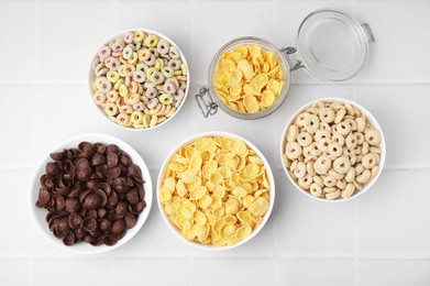 Photo of Different delicious breakfast cereals on white tiled table, flat lay