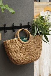 Stylish beach bag with beautiful wildflowers and books hanging on dark grey wall