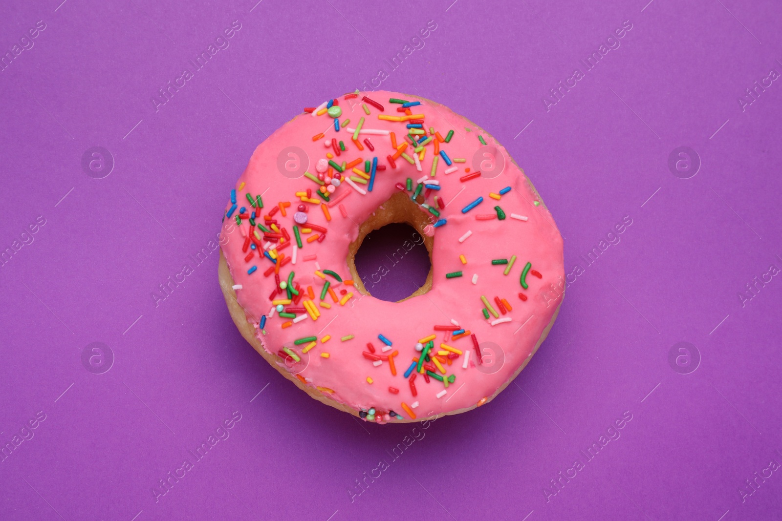 Photo of Sweet glazed donut decorated with sprinkles on purple background, top view. Tasty confectionery