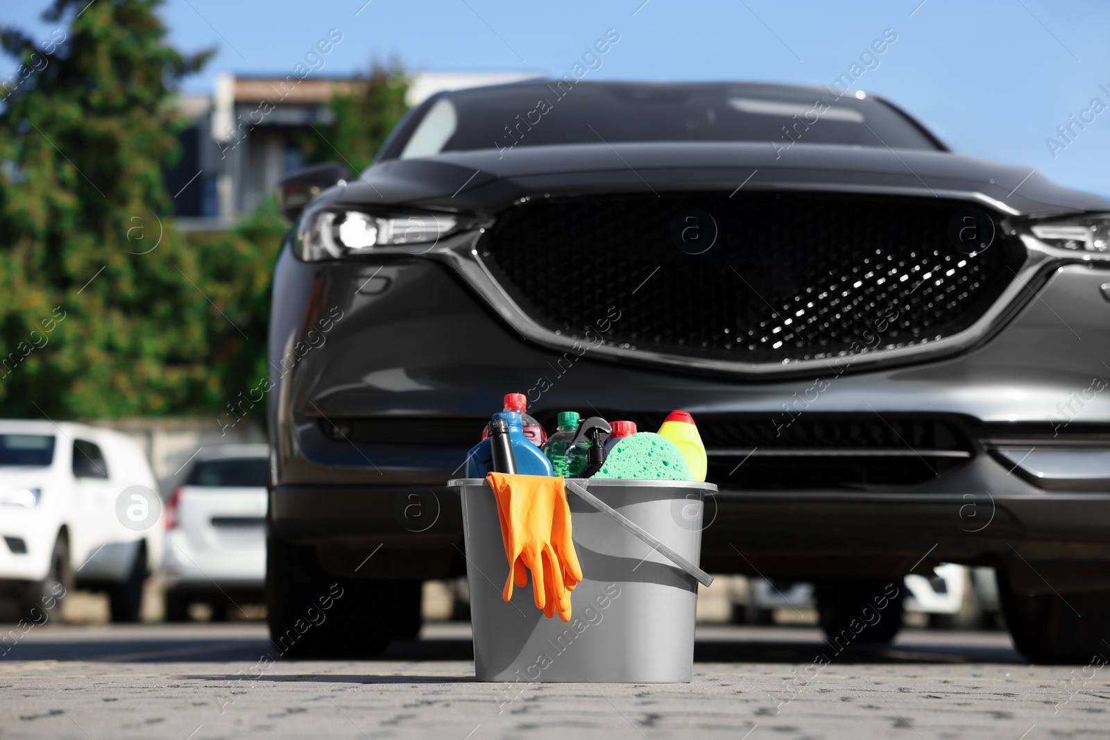 Photo of Car cleaning products in bucket near automobile outdoors on sunny day