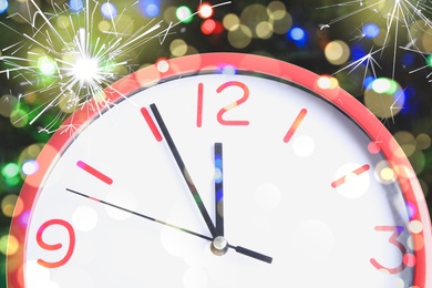 Clock showing five minutes till midnight with sparklers, closeup with bokeh effect. New Year countdown