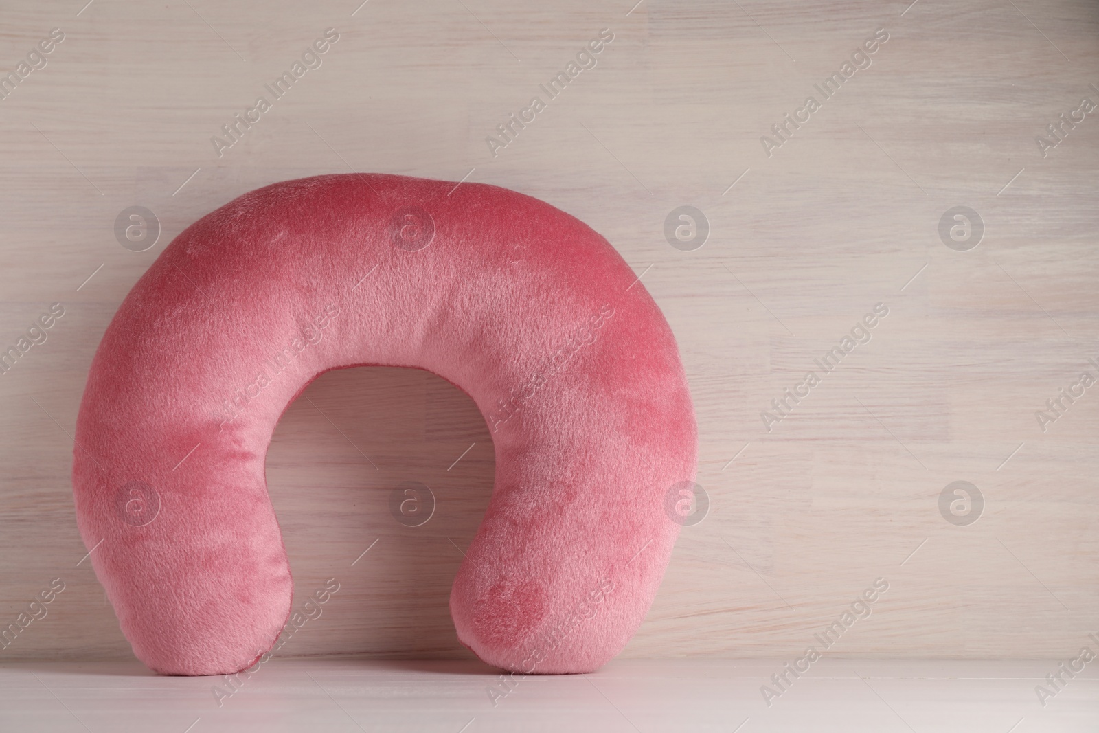 Photo of Pink travel pillow on light wooden background, space for text