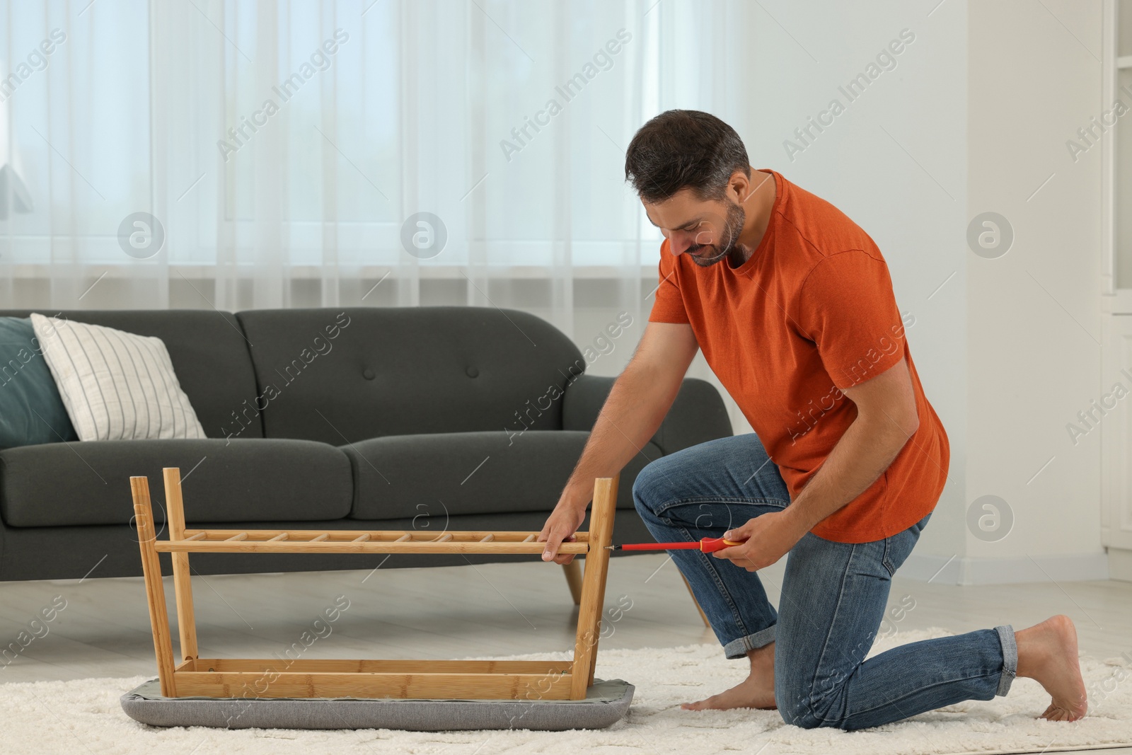 Photo of Man assembling shoe storage bench with screwdriver on floor at home