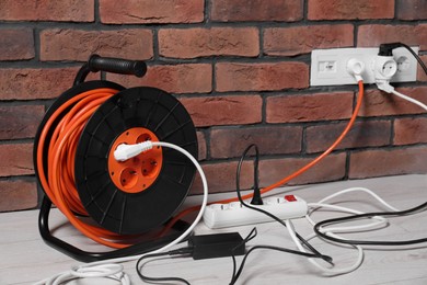Photo of Extension cord reel plugged into socket on white laminated floor near brick. Electrician's equipment