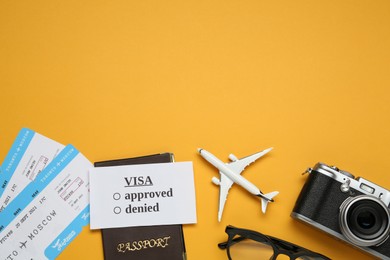 Photo of Flat lay composition with passport, toy plane and camera on orange background, space for text. Visa receiving