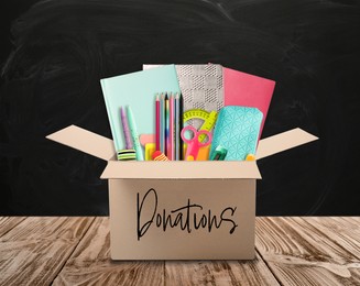 Image of Donation box with different school stationery on wooden table near blackboard