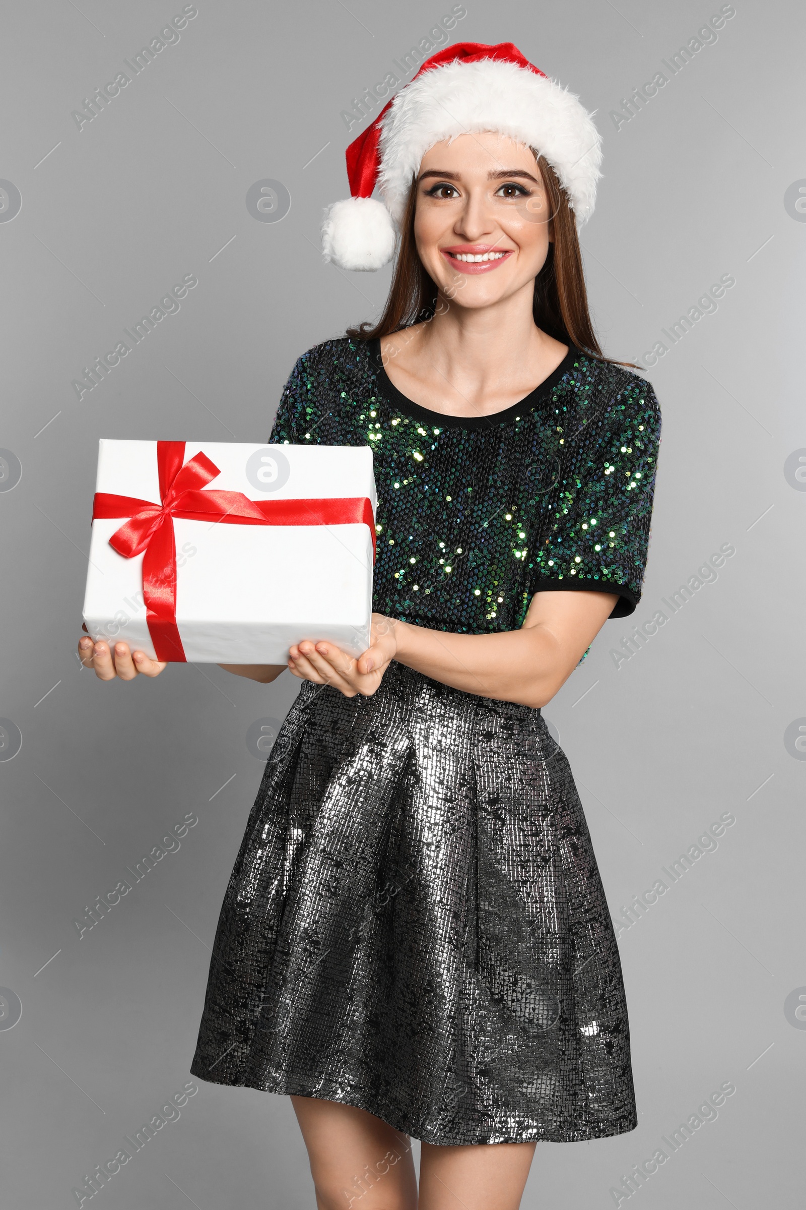 Photo of Happy young woman in Santa hat with gift box on light grey background. Christmas celebration