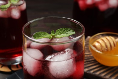 Refreshing hibiscus tea with ice cubes and mint in glass on table, closeup
