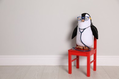 Photo of Toy penguin with eyeglasses and stethoscope near white wall, space for text. Pediatrician practice