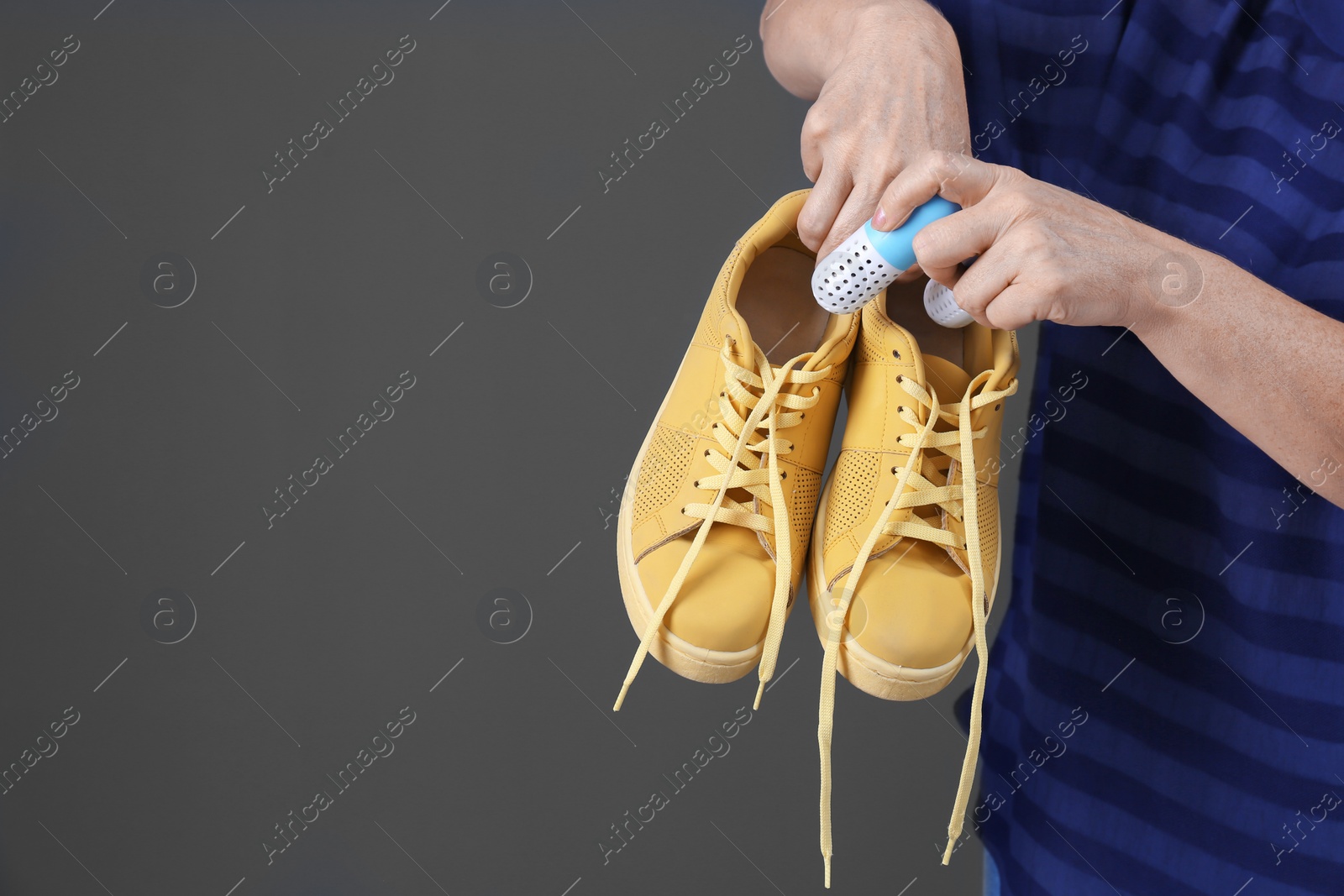 Photo of Woman putting capsule shoe freshener in footwear on color background, closeup