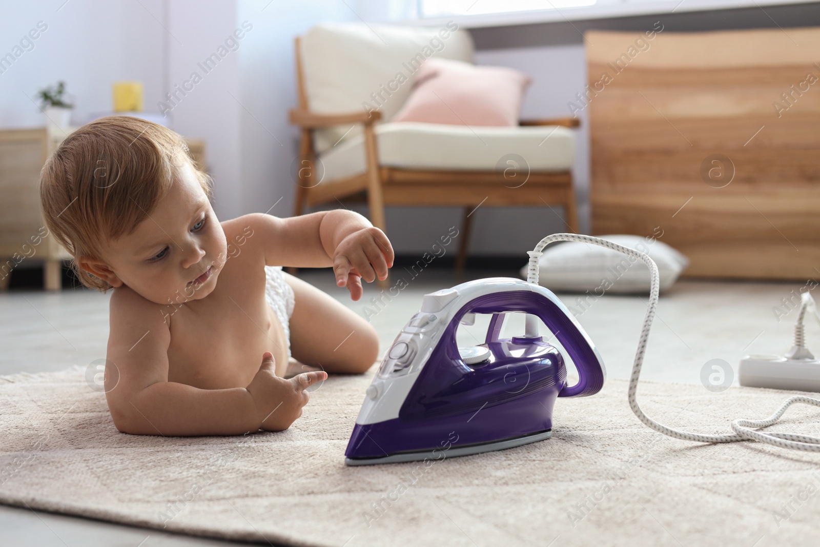 Photo of Cute baby playing with iron on floor at home. Dangerous situation