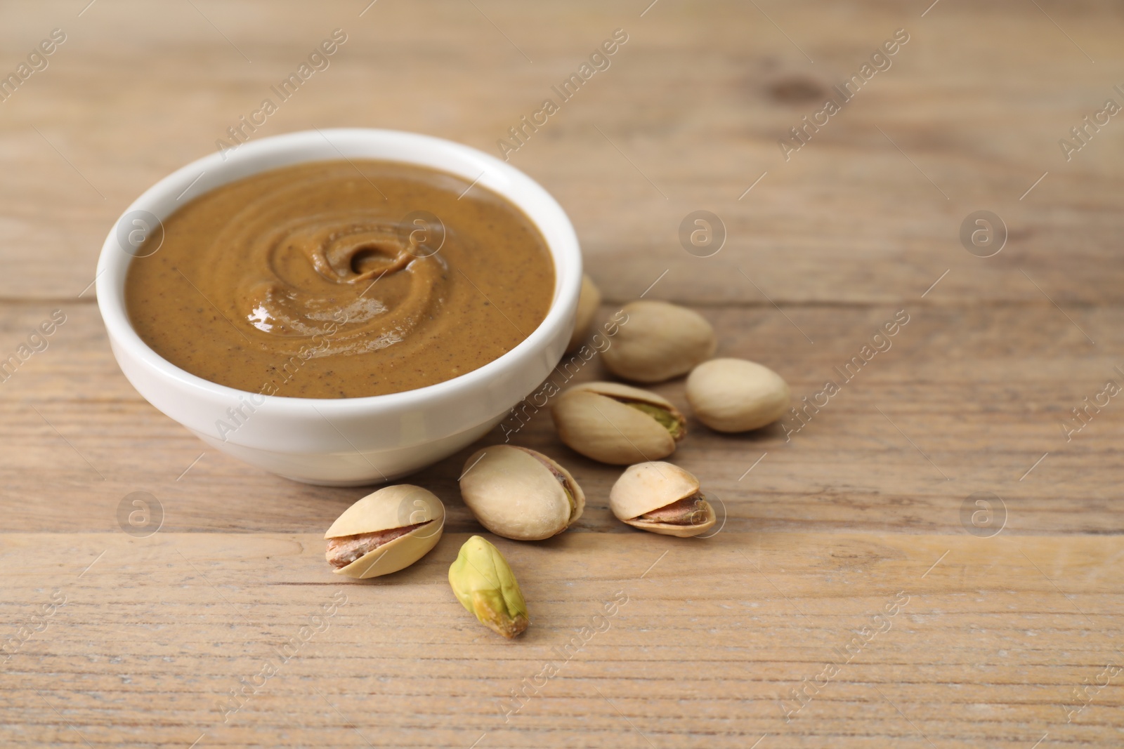 Photo of Delicious nut butter in bowl and pistachios on wooden table