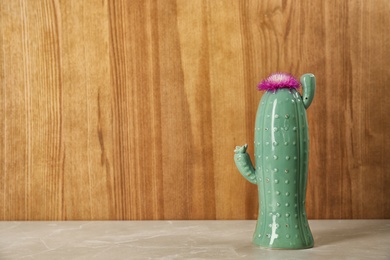 Photo of Trendy cactus shaped ceramic vase with flower on table against wooden background