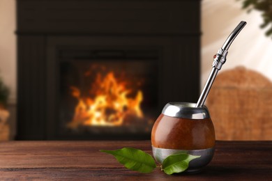 Image of Calabash with mate tea and bombilla on wooden table near fireplace. Space for text