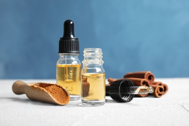 Photo of Bottles of essential oils, cinnamon sticks and powder on table against blue background