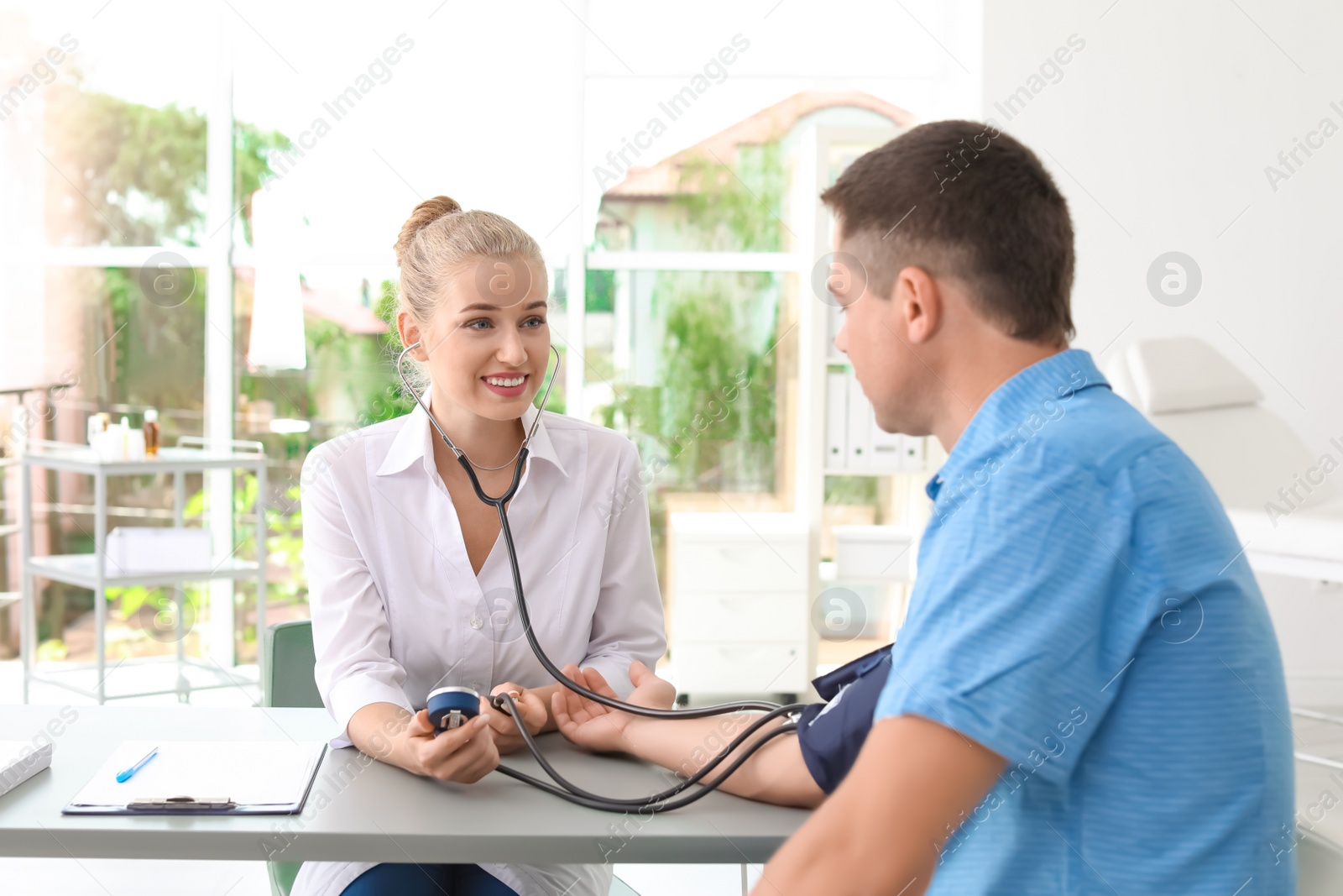 Photo of Doctor checking patient's blood pressure at table in office