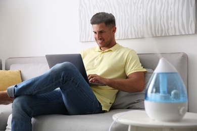 Photo of Man using laptop in room with modern air humidifier