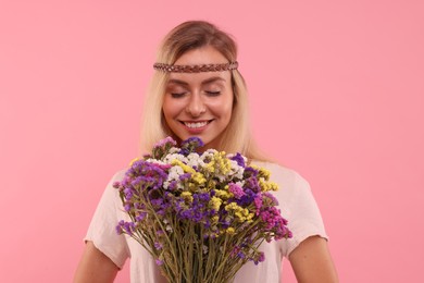 Portrait of smiling hippie woman with bouquet of flowers on pink background