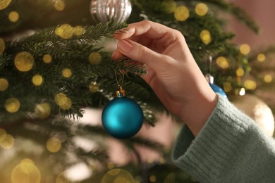 Photo of Woman decorating Christmas tree with beautiful light blue bauble, closeup