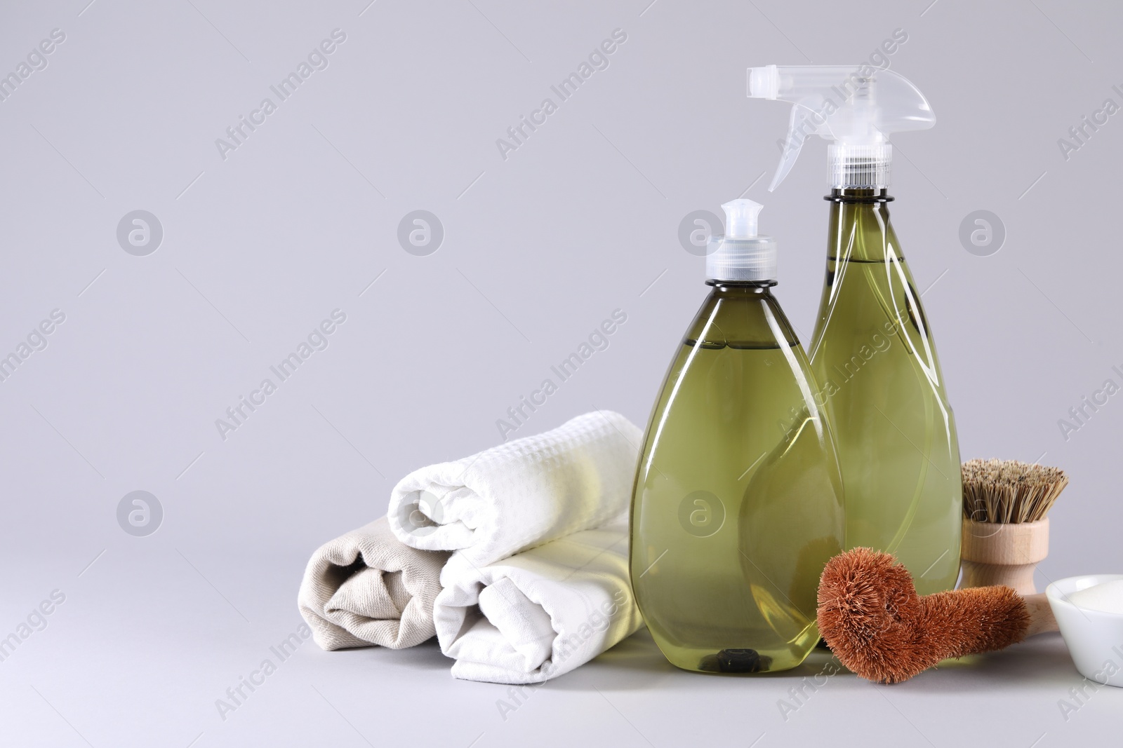 Photo of Bottles of cleaning product, brushes, rags and baking soda on light background. Space for text