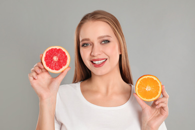 Young woman with cut orange and grapefruit on grey background. Vitamin rich food