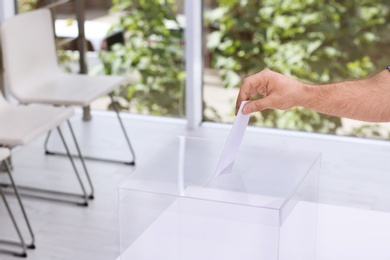 Man putting his vote into ballot box at polling station, closeup